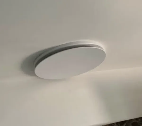 Round low-profile exhaust fan in a bathroom ceiling above dark marble tiles