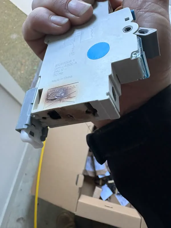 Old circuit breaker with burn marks on its casing, held in a hand after removal