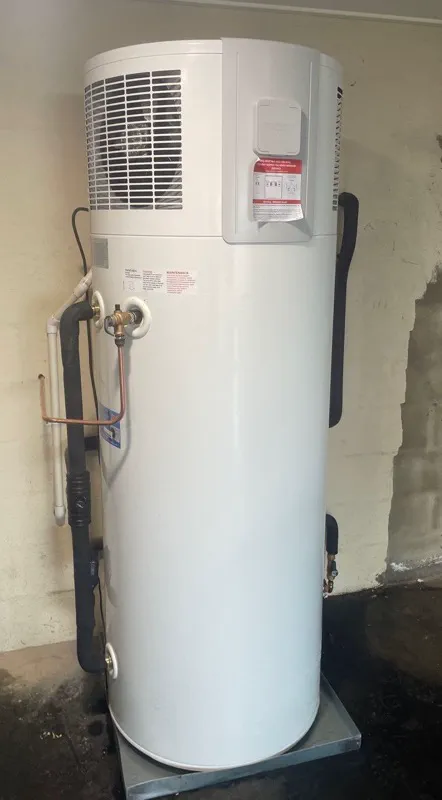 All-in-one heat pump hot water unit standing on a safe tray in a garage corner