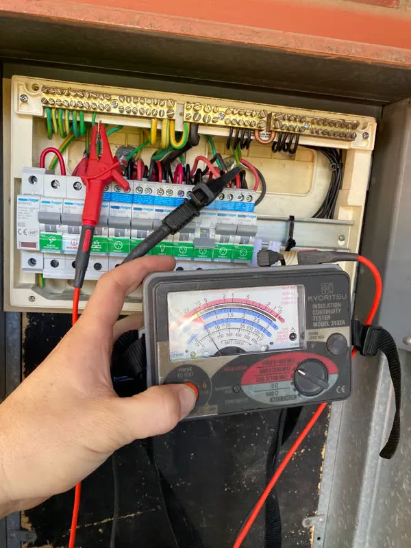Kyoritsu insulation tester clipped to a switchboard in an outdoor meter box