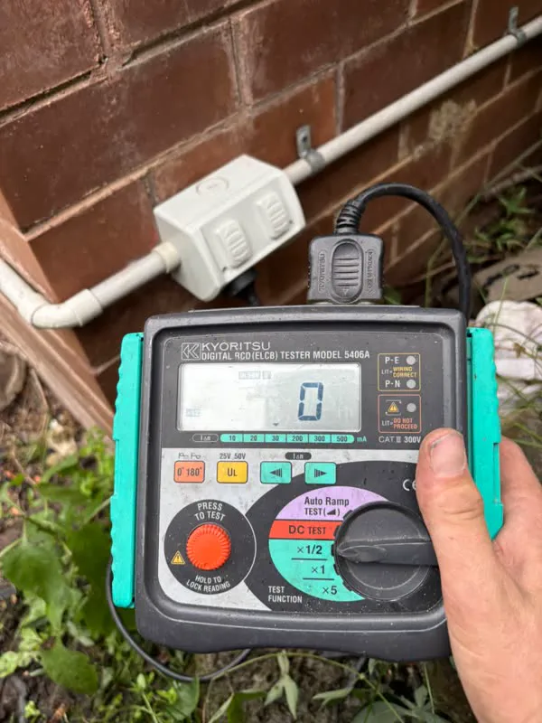 Kyoritsu RCD tester plugged into a weatherproof outdoor power point on a brick wall