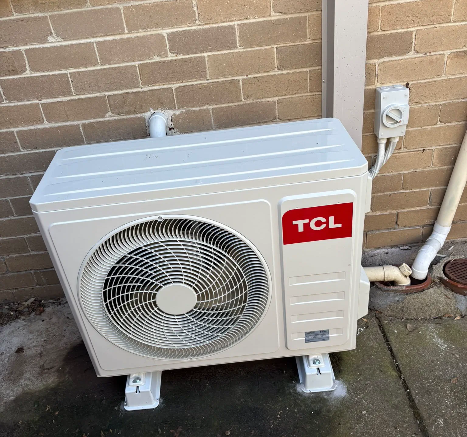 TCL split system outdoor unit on anti-vibration feet beside a weatherproof isolator switch