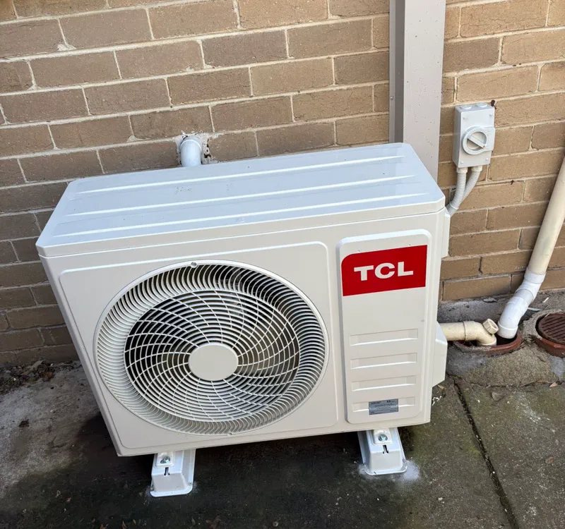 TCL split system outdoor unit on anti-vibration feet beside a weatherproof isolator switch