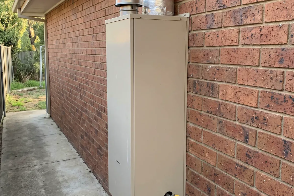 An external gas ducted heater on a brick wall, with its flue cap, insulated duct and gas valve