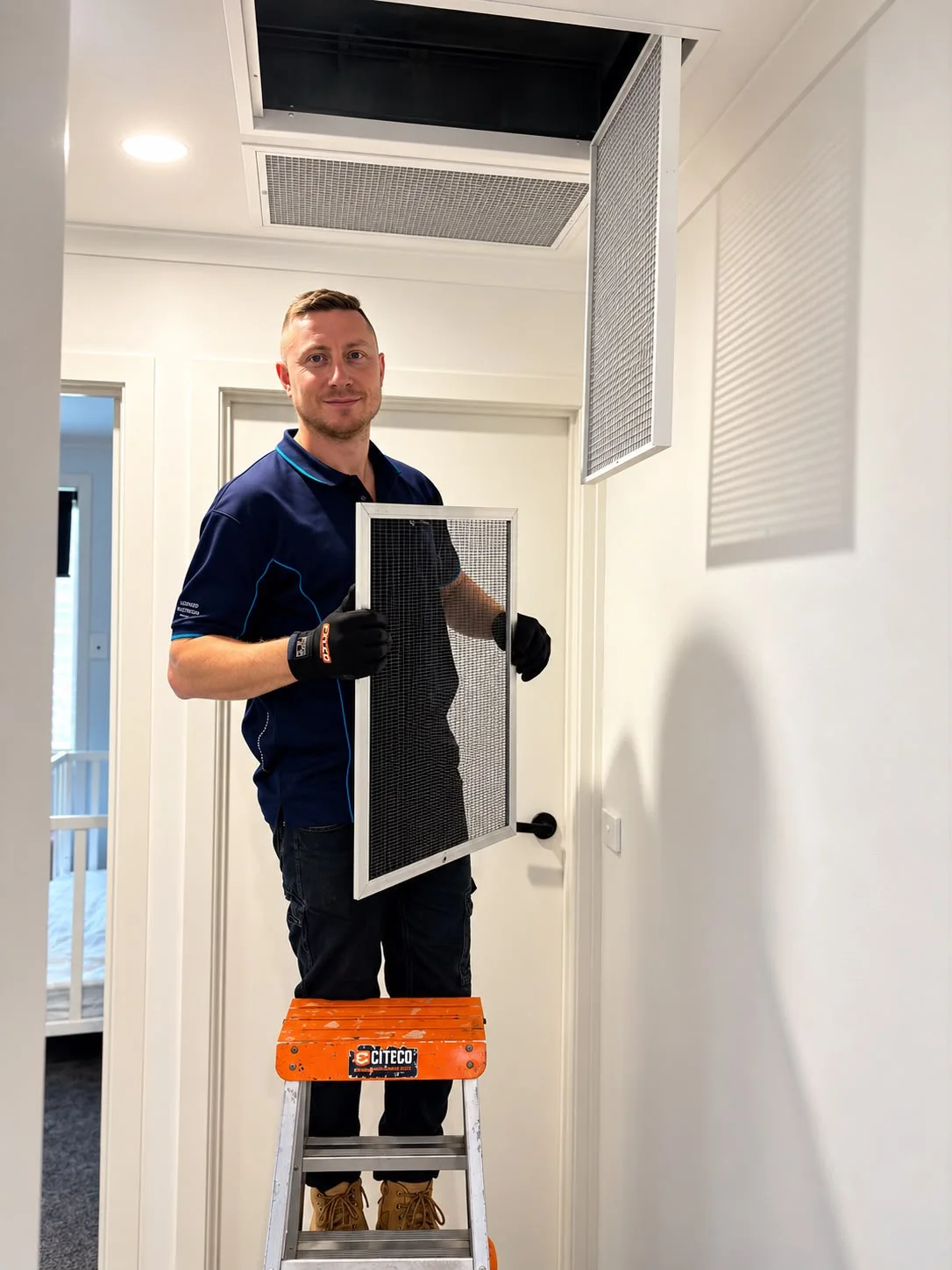 Total Comfort technician holding a removed return-air filter beside a ladder